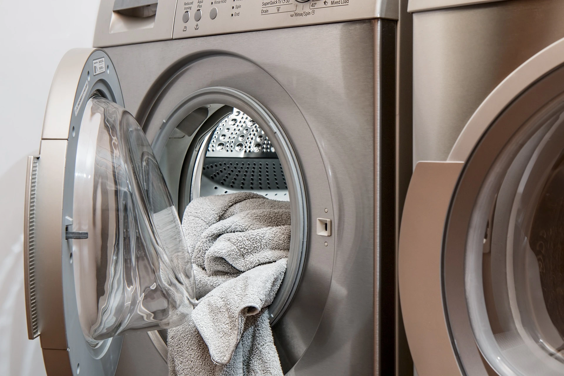 Lavatrice con portellone aperto e asciugamano grigio che penzola fuori dal cestello - immagine di copertina